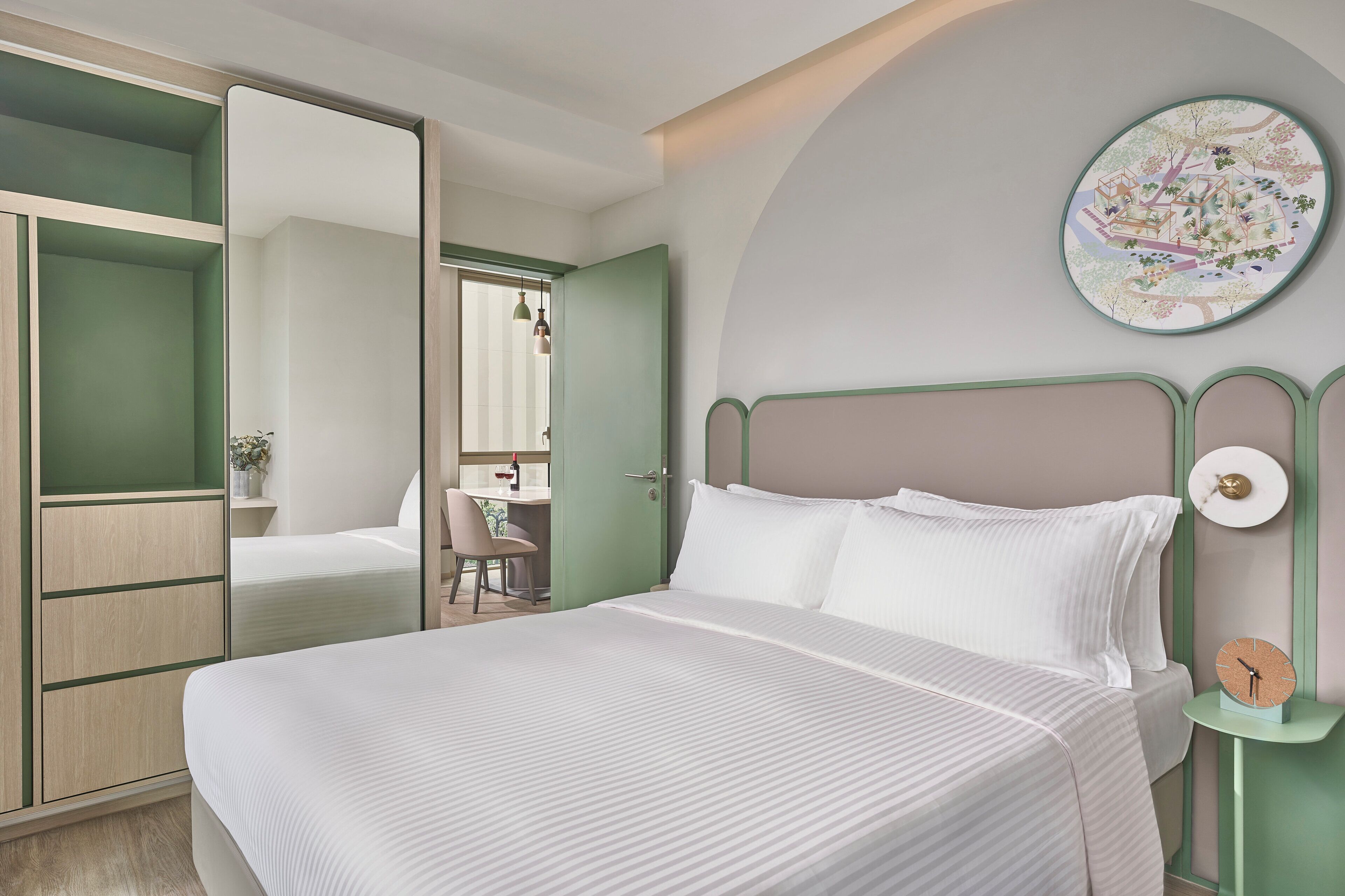 A neatly arranged bedroom with a bed, a bedside table with a clock, and a green-framed wardrobe.