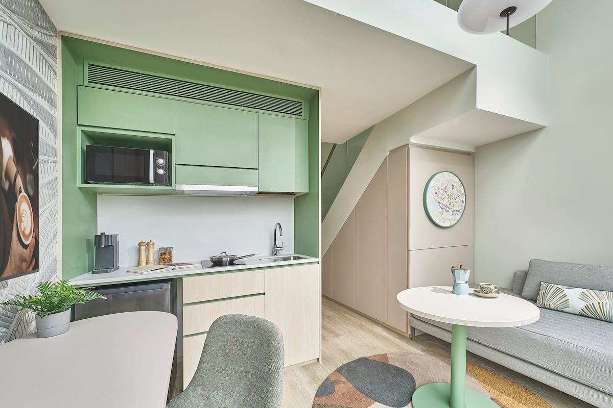 Une cuisine compacte avec des meubles de couleur verte, un four à micro-ondes et une machine à café. On y trouve un coin repas avec une table et des chaises, ainsi qu'un canapé dans l'espace de vie.