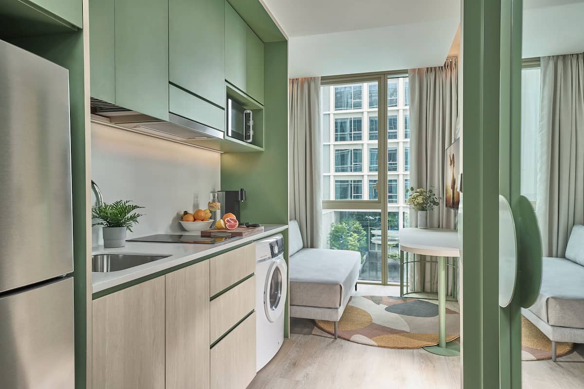 Une cuisine compacte équipée d’un lave-linge, d’un four à micro-ondes et d’un évier. On y trouve également un coin repas avec une table et des chaises, ainsi qu’une grande fenêtre offrant une vue sur la ville.