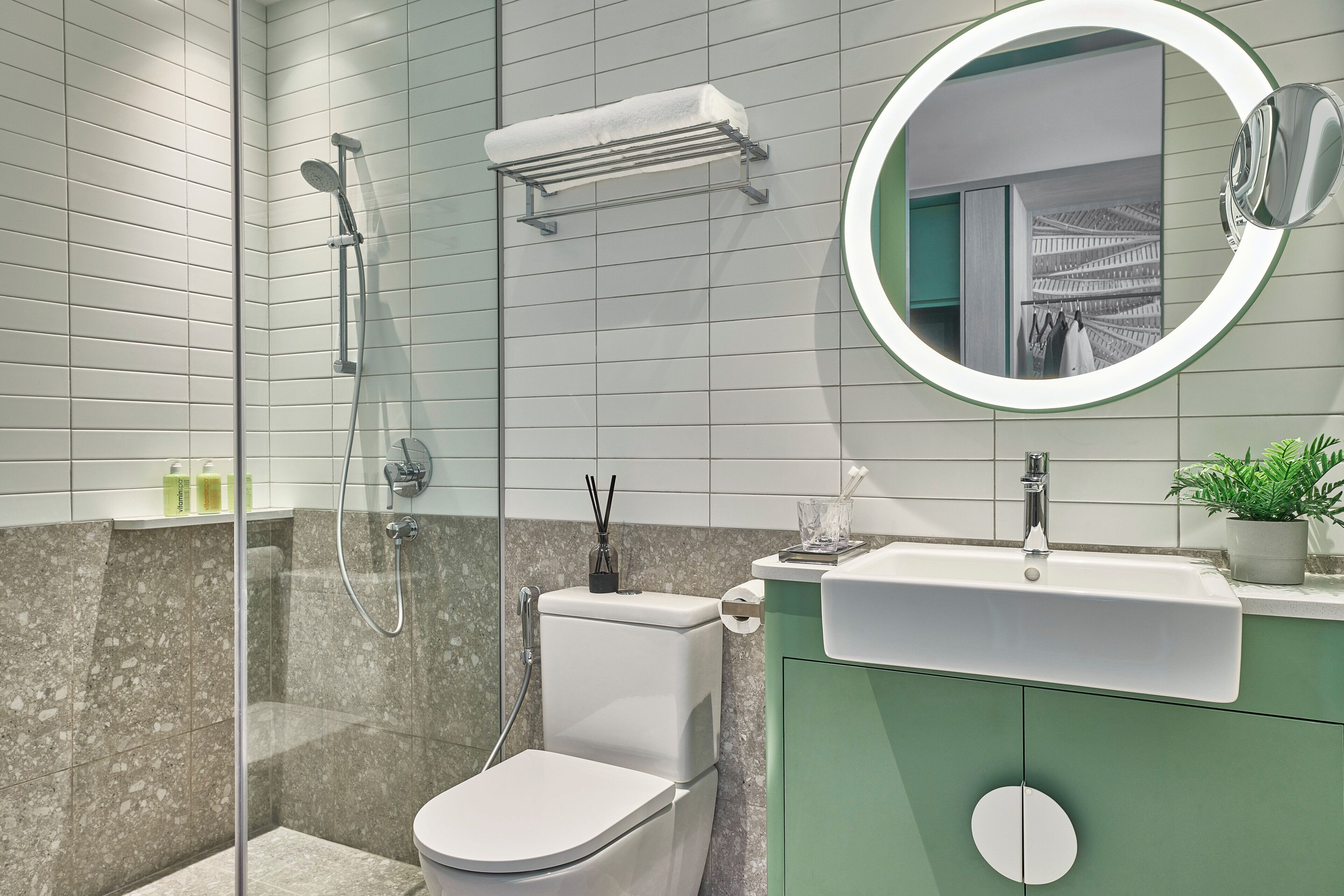 Un bagno moderno con cabina doccia in vetro, un water, un lavabo con specchio e un mobile contenitore verde.