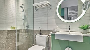 Un baño moderno con ducha envuelta en vidrio, inodoro, lavabo con espejo y tocador verde.