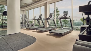 Un gimnasio con cintas de correr, bicicletas estáticas y máquinas de pesas, grandes ventanales y vistas a la ciudad.