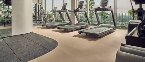 A gym with treadmills, exercise bikes, and weight machines, large windows, and a view of the city.