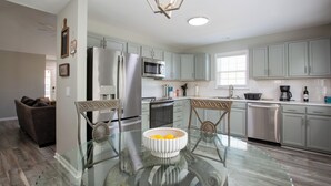 A modern kitchen with light grey cabinets, stainless steel appliances, and a glass dining table.