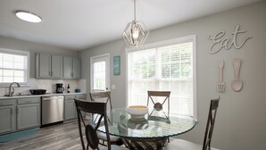 A modern kitchen with a glass dining table, wooden chairs, and a pendant light.