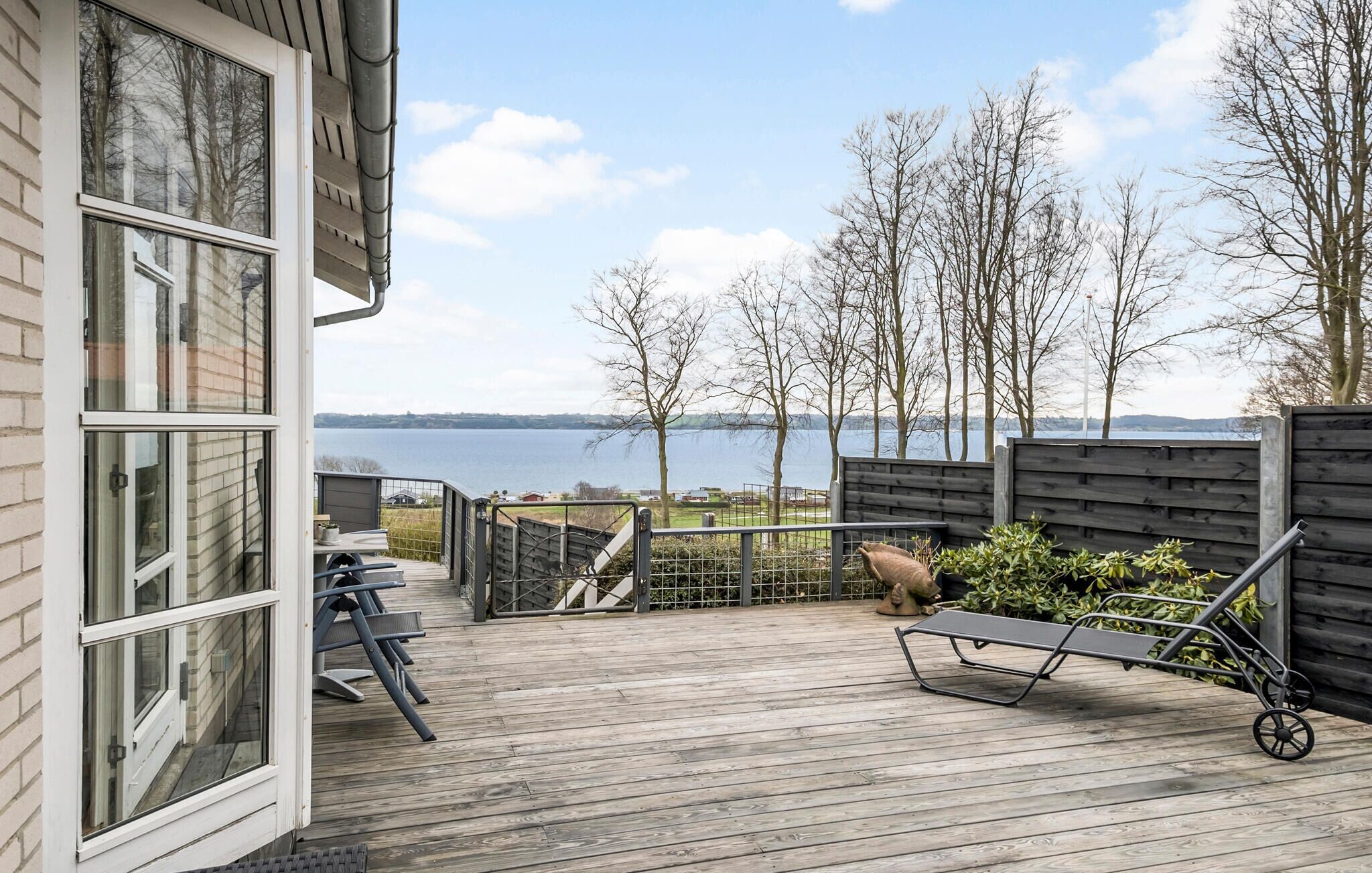 Une terrasse en bois offrant une vue sur un lac, un banc en métal et une statue.