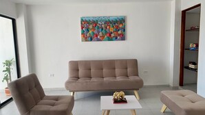 A modern living room with a brown sofa, two matching armchairs, and a small table with a decorative elephant figurine. A colorful abstract painting is on the wall. - «Javi's house: explore the charm of Cartagena (Cartagena de Indias)
