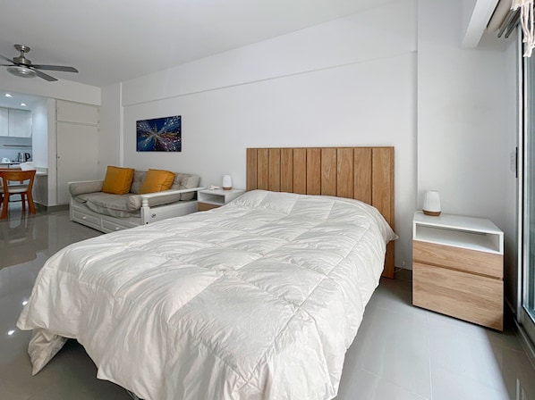 A modern bedroom with a large bed, a wooden headboard, a bedside table, and a small desk with a chair.