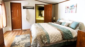 Un dormitorio con cama, piso de madera, ventilador de techo y una puerta que da al baño.