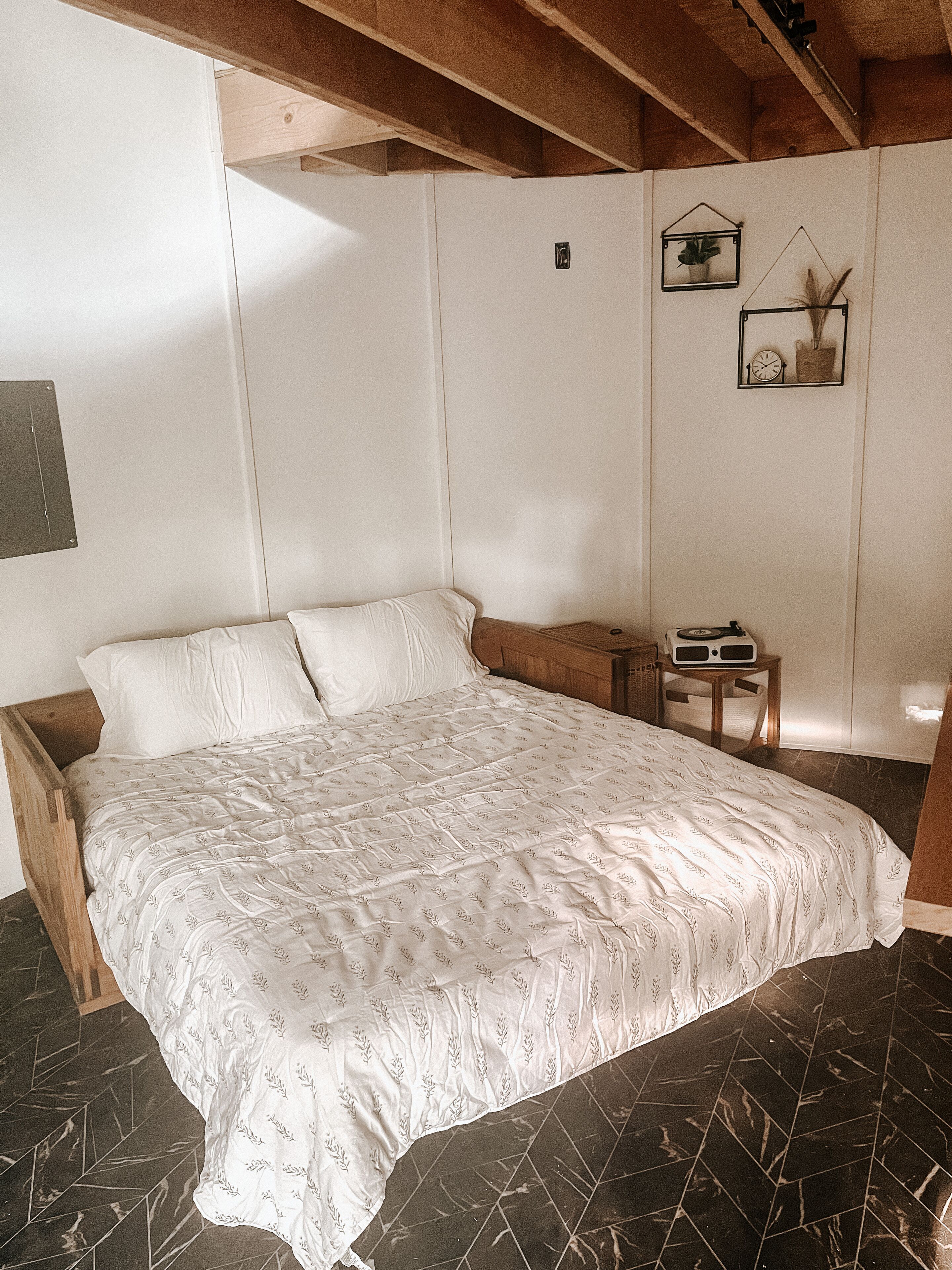 A bedroom with a large bed, a small bedside table, and a wall-mounted clock.