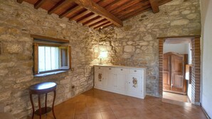 A stone-walled kitchen with a window, a white cabinet, and a wooden stool.