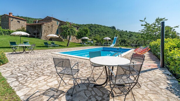 A pool area with stone flooring, lounge chairs, and umbrellas.
