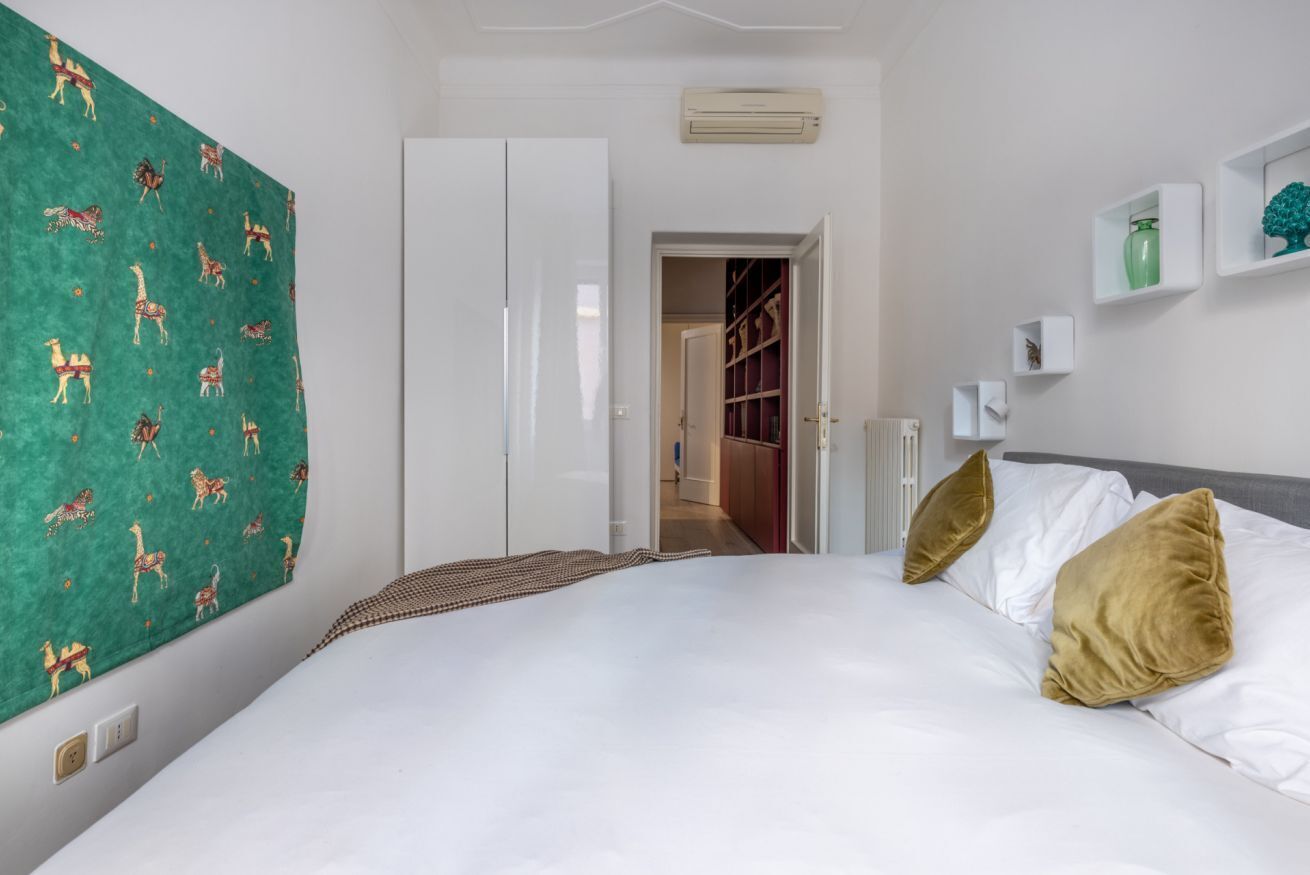 Une chambre à coucher comprenant un lit, une armoire, un mur à motifs verts et un couloir menant à une pièce dont la porte est rouge.