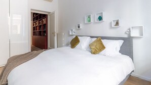 A neatly arranged bedroom with a large bed, a wardrobe, and a small shelf with decorative items.