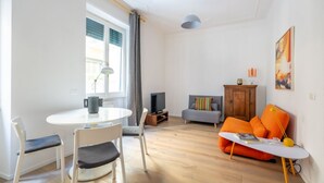 A modern living room with a round table, two chairs, a grey sofa, and a television.