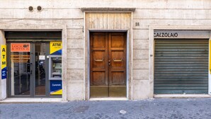A building facade with a closed shutter on the right and a door with a sign above it.