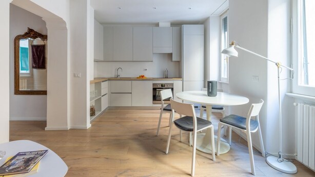 A modern kitchen with white cabinets, a round dining table with two chairs, and a floor lamp.