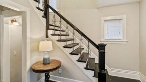 En trappe med gelænder i sort metal og metalspind, et rundt træbord med en lampe, og et vindue med persienner.