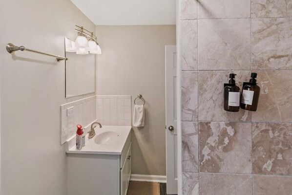 A bathroom with a sink, mirror, towel rack, and two shampoo bottles on the wall.