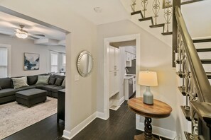 A living room with a sectional sofa, a round mirror, and a lamp near a staircase.