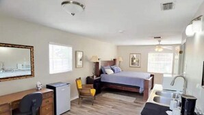 Une chambre d’hôtel de taille réduite, comprenant un lit, un bureau, une chaise et une kitchenette.