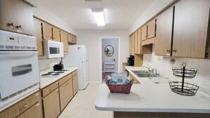 Une cuisine compacte dotée de meubles en bois, d’un four à micro-ondes, d’une cuisinière, d’un réfrigérateur, d’un évier et d’un petit îlot central avec un panier.
