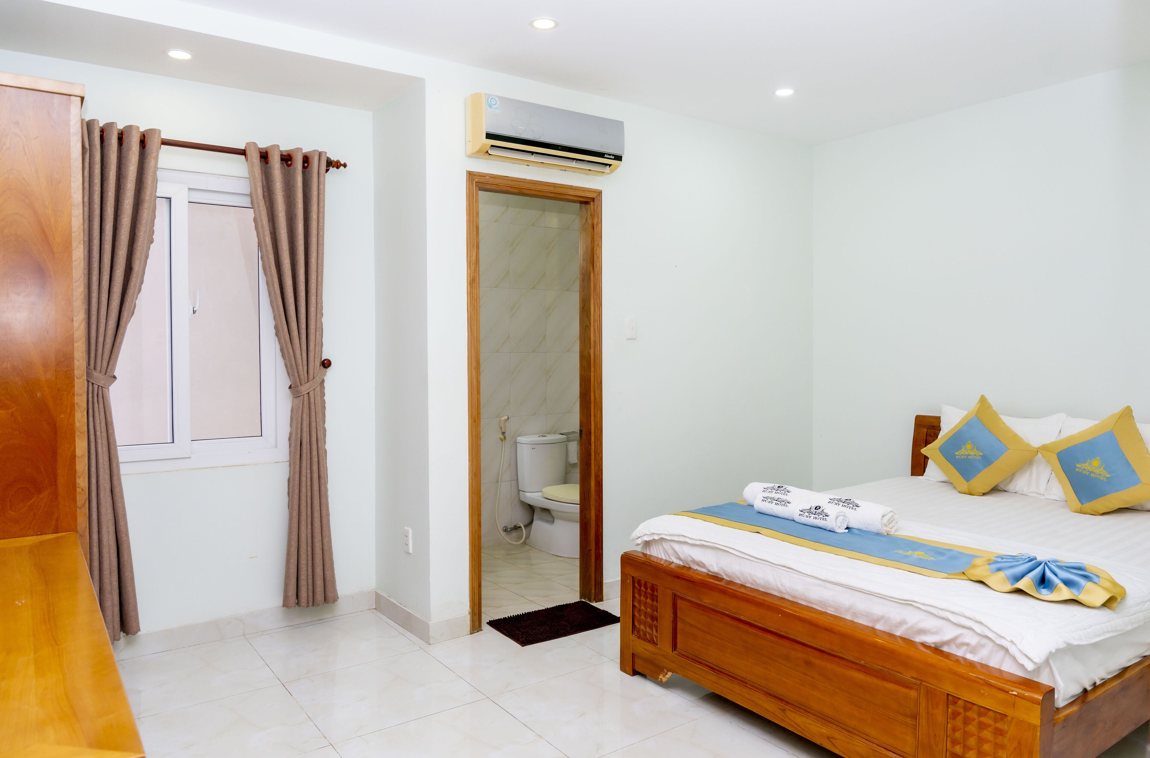 A hotel room with a wooden bed, a bathroom door, and an air conditioning unit.