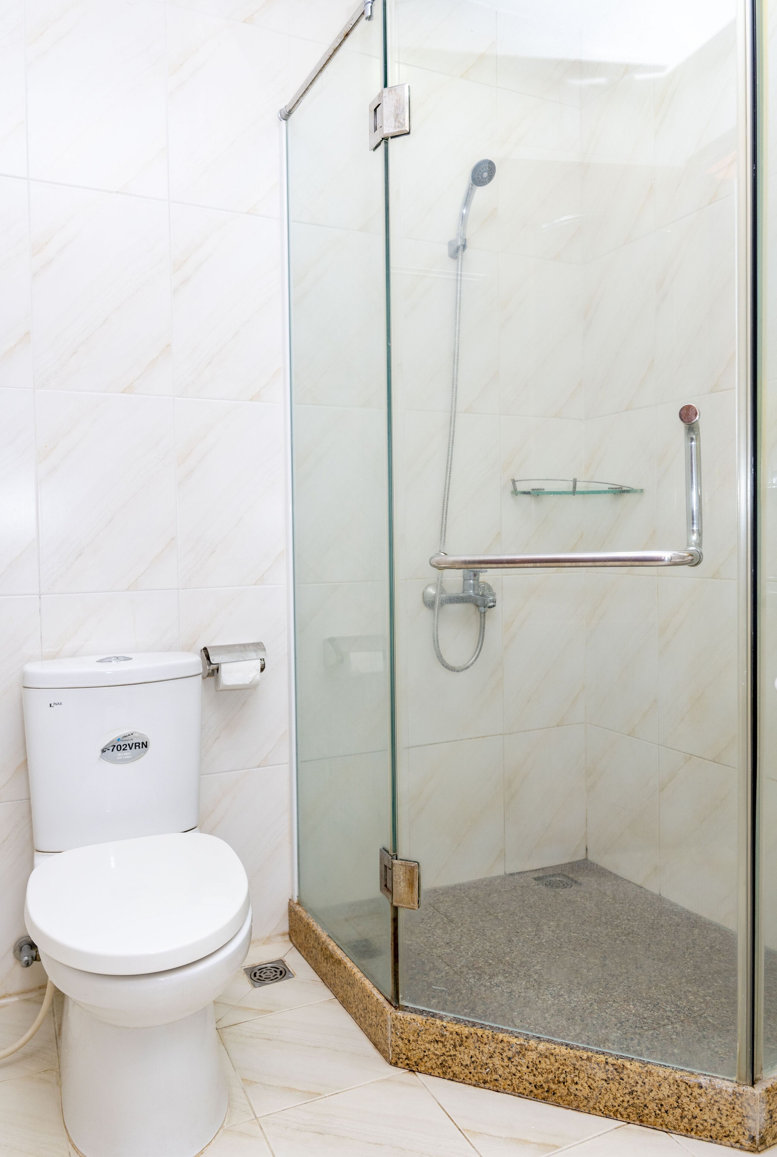 Une salle de bain comprenant des toilettes, une douche à parois de verre et une étagère en verre.
