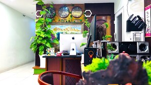Een werkplek aan huis met een bureau, computer en speakers. Tegen de muur hangen klokken en in de hoek staat een plant.