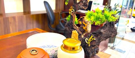 Una mesa de madera con una escultura de árbol decorativa, una maceta de cerámica blanca y un bidón de gas naranja.