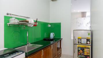 Eine kompakte Küche mit grüner Rückwand, einem Edelstahlspüle, einem weißen Kühlschrank und einer Mikrowelle.