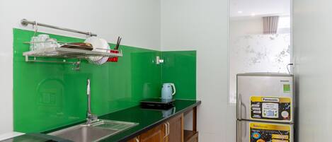 A compact kitchen with a green backsplash, a stainless steel sink, a white refrigerator, and a microwave.