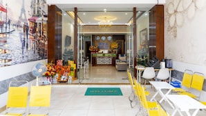 Een hotellobby met een receptiebalie, een 'Welcome'-mat, zitgedeeltes en een muurschildering van Parijs.