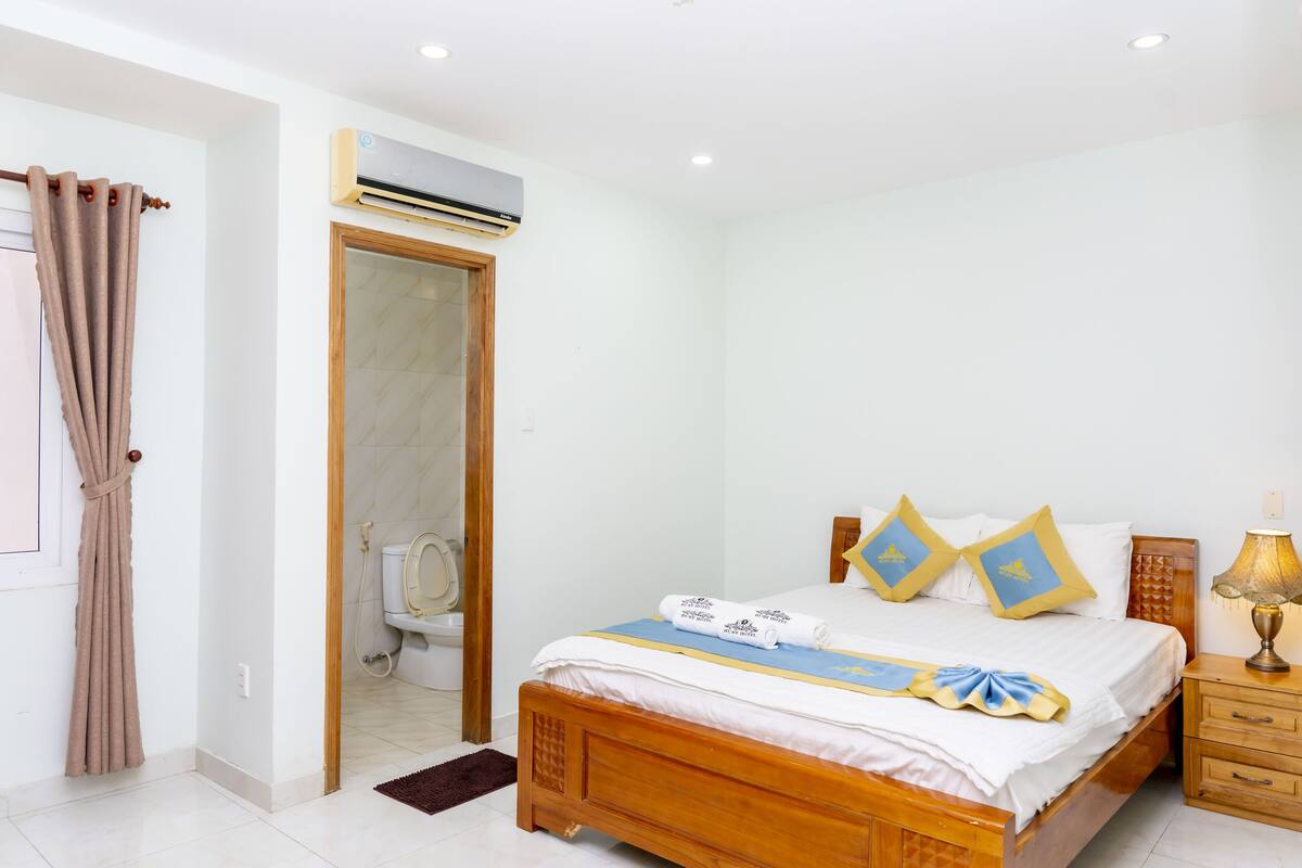 A bedroom with a wooden bed, a nightstand, a lamp, and an air conditioning unit.