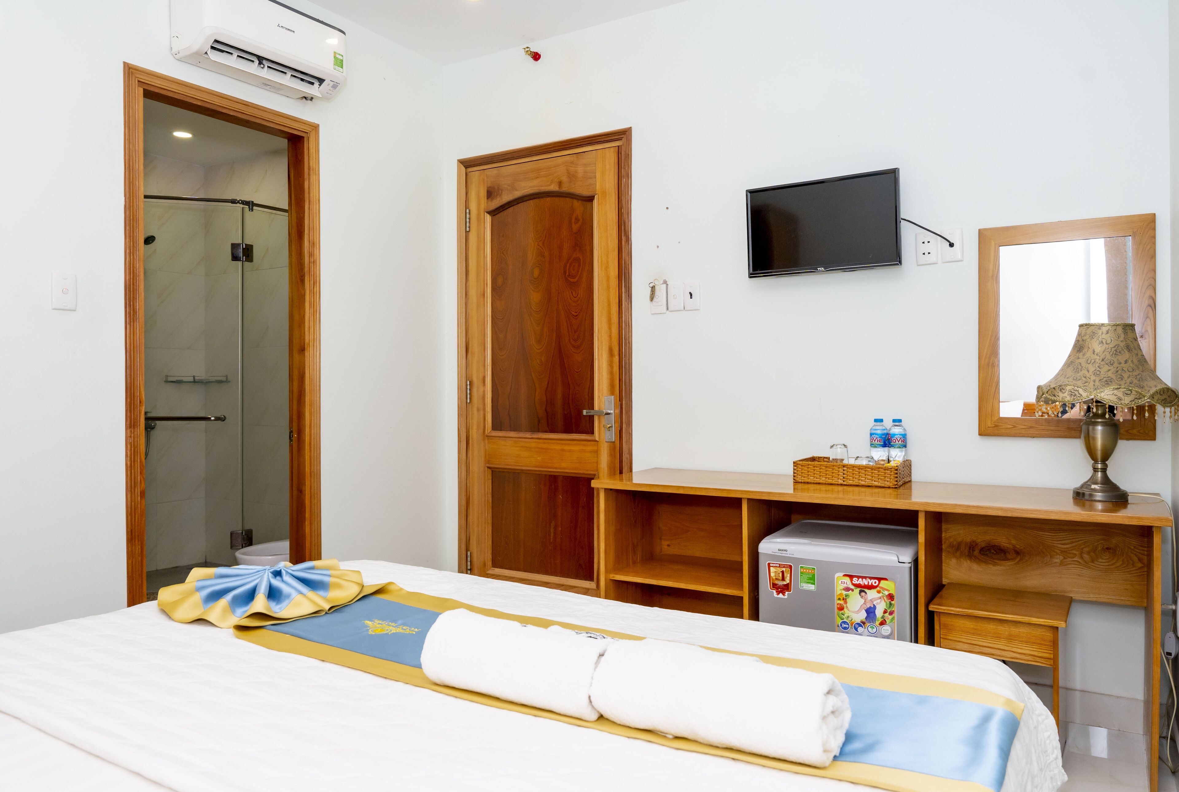 A hotel room with a bed, a wooden wardrobe, a television, a refrigerator, and a shower.