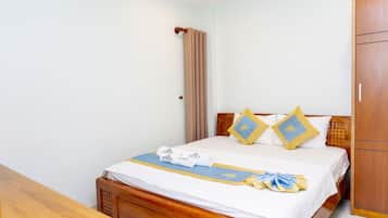 Cama bem arrumada com edredom branco e azul, dois travesseiros combinando e cabeceira de madeira.