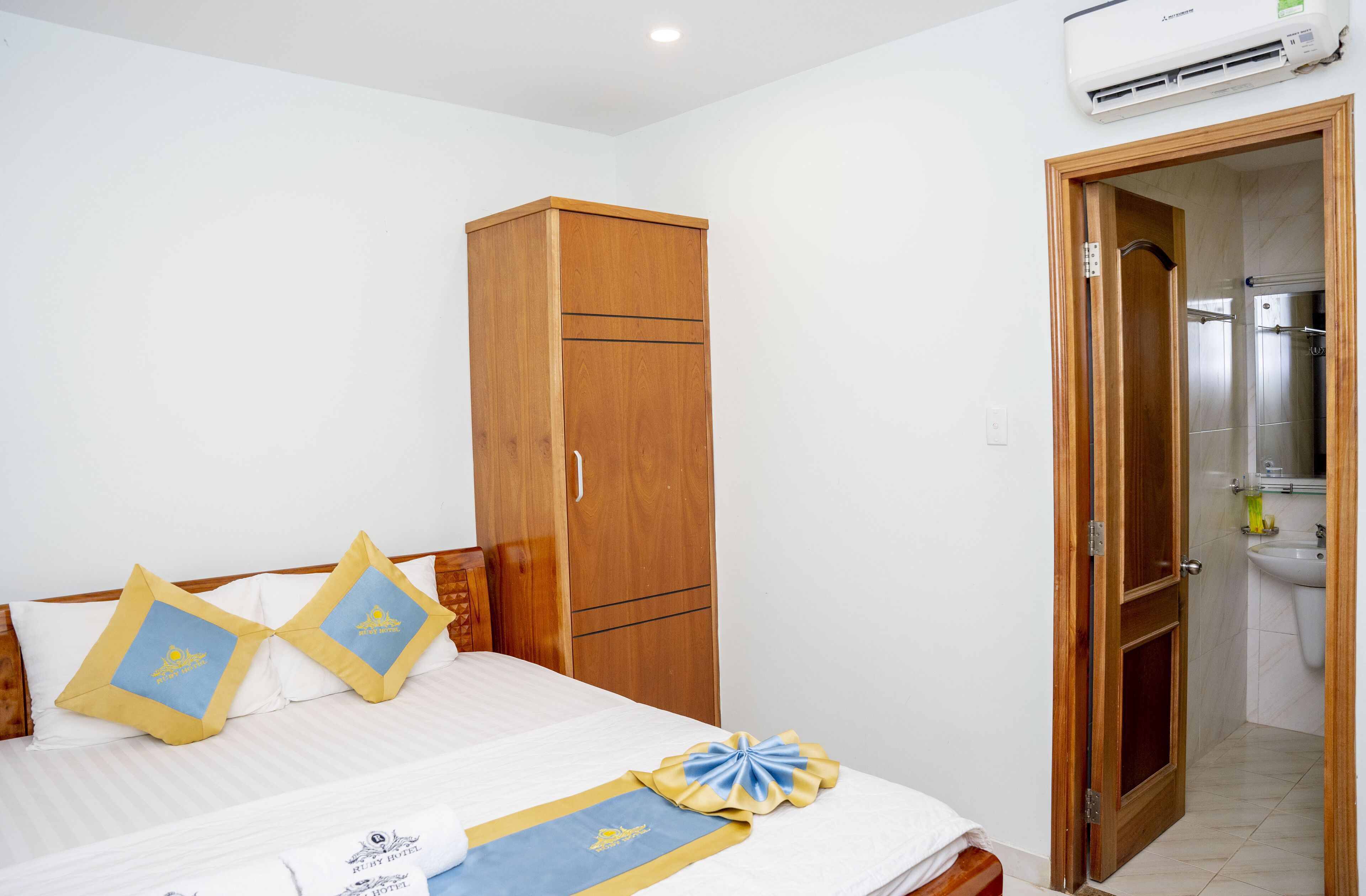 A hotel room with a bed, wooden wardrobe, and a bathroom visible through an open door.