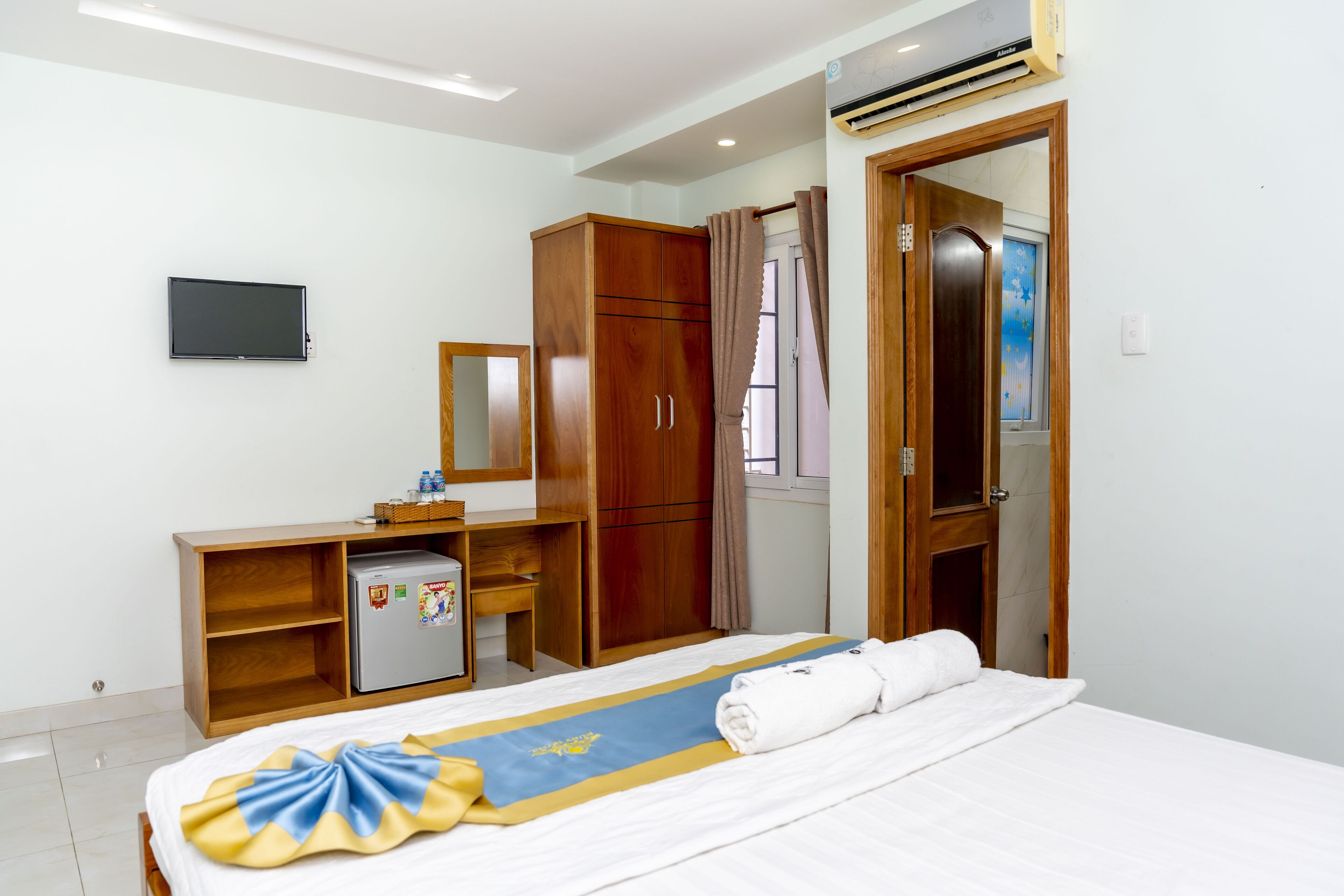 A hotel room with a bed, a desk, a wardrobe, a television, and an air conditioning unit.