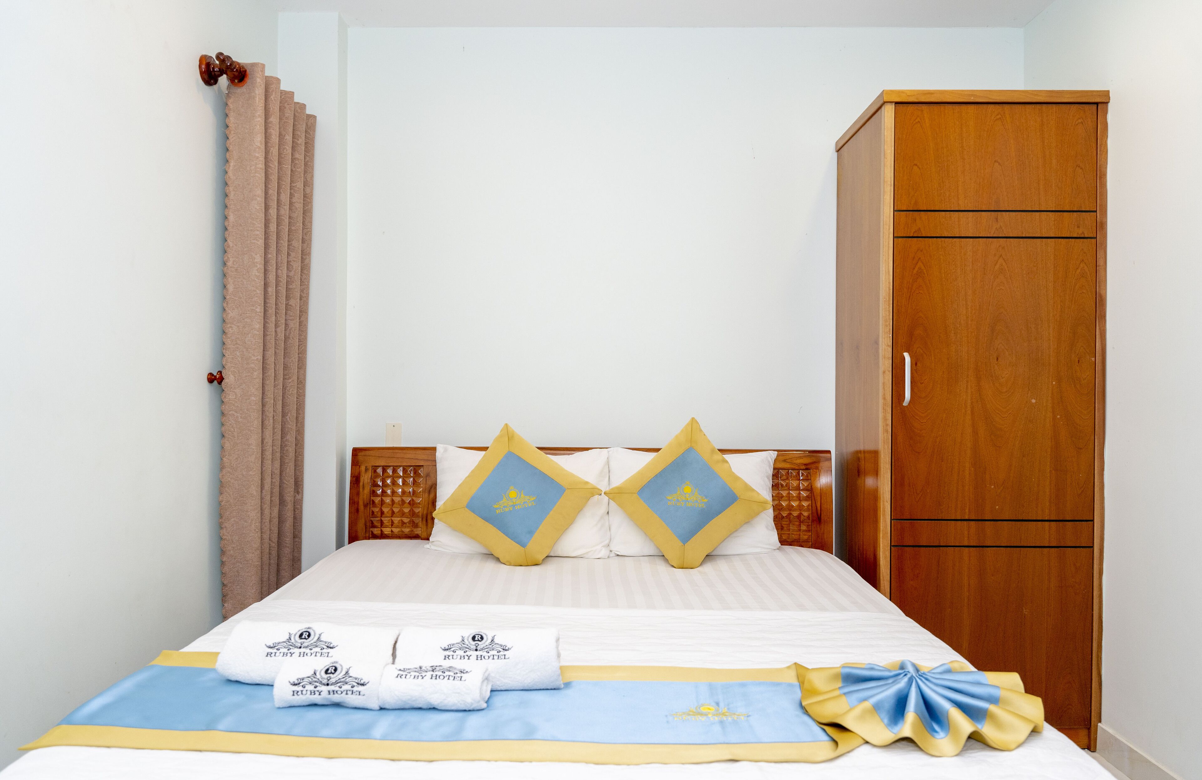 Een hotelkamer met een bed, twee kussens, een houten garderobe en een gordijn.