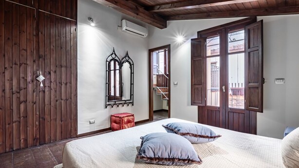 Un dormitorio con techo de madera, una cama con dos almohadas, un taburete rojo y un espejo en la pared.
