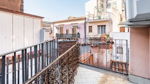 Un callejón estrecho con barandilla metálica, edificios adyacentes con balcones y un cielo despejado.