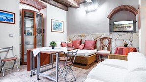 Una habitación con cama, una mesa de comedor, sillas, un aparador de vidrio, un televisor y una pared de piedra.