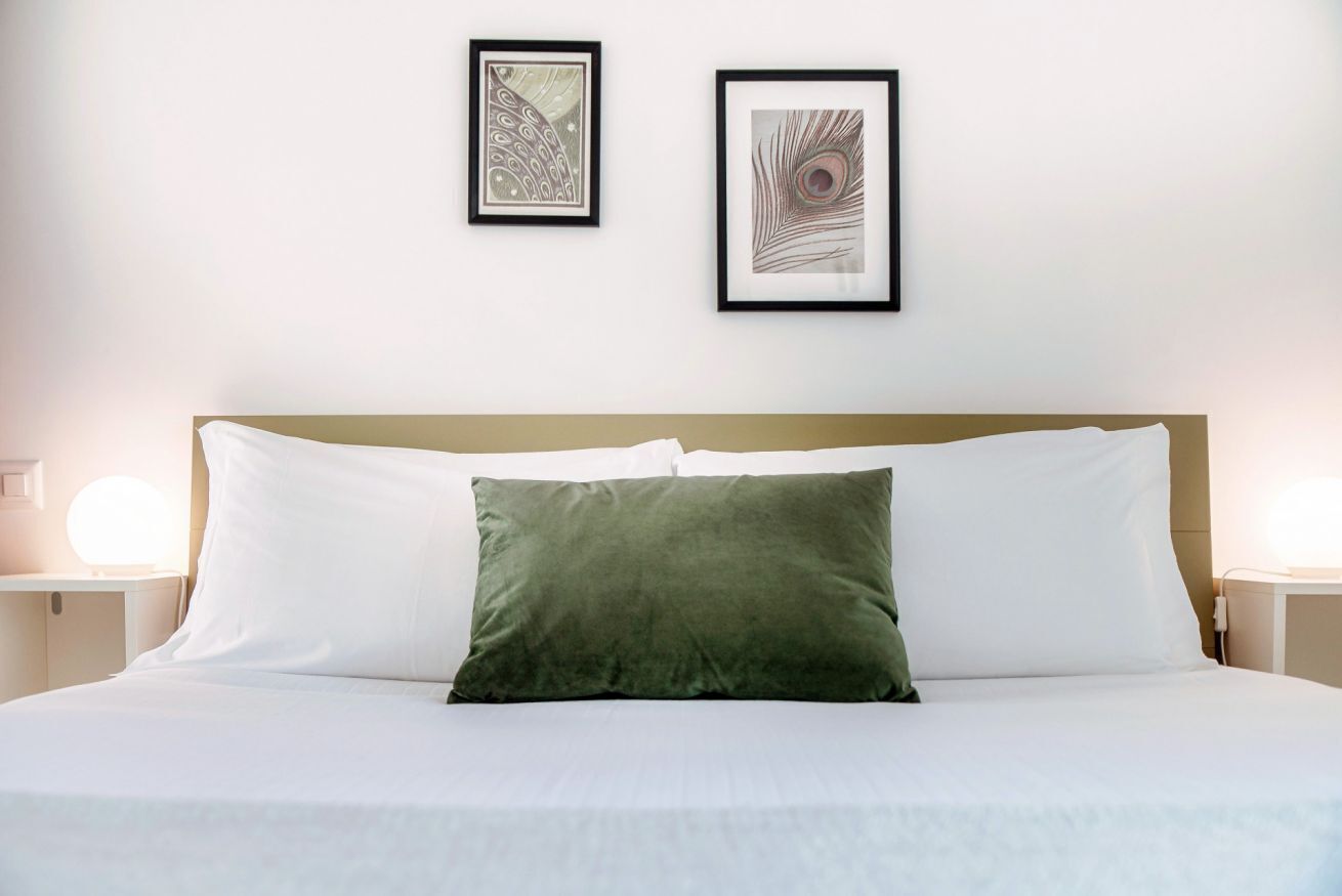 A neatly made bed with white and green pillows, two framed artworks on the wall, and bedside lamps.