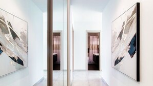 Ein Flur mit Spiegelwänden und abstrakten Gemälden, der zu einem Raum mit Dusche und WC führt.