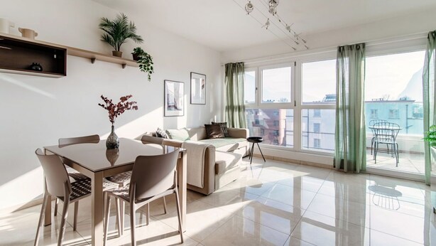 Ein modernes Wohnzimmer mit Essbereich, großen Fenstern und Blick auf eine Stadtlandschaft.