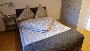 Una cama bien hecha con ropa de cama estampada, una lámpara de noche y una mesita de noche con un teléfono.