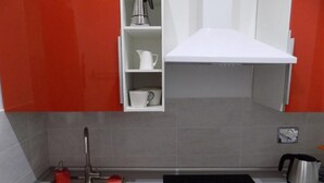Een keuken met een wit aanrecht, een roestvrijstalen spoelbak en een rode waterkoker.