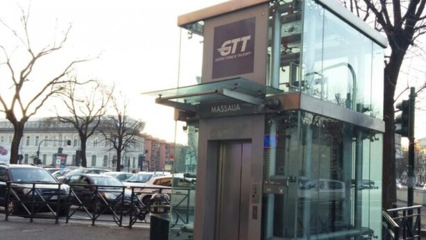 Een moderne glazen liftinrichting met de aanduiding 'MASSAUA' en het logo 'STT' erboven.