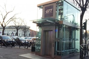 Una entrada moderna de ascensor de vidrio con la etiqueta 'MASSAUA' y el logotipo 'STT' en la parte superior.