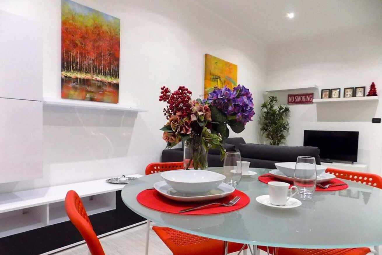 A modern dining area with a glass table, red chairs, a vase with flowers, and a 'NO SMOKING' sign on the wall.